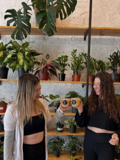 Two guests toasting branded Wooden Cow Coffee iced lattes in a plant-filled studio