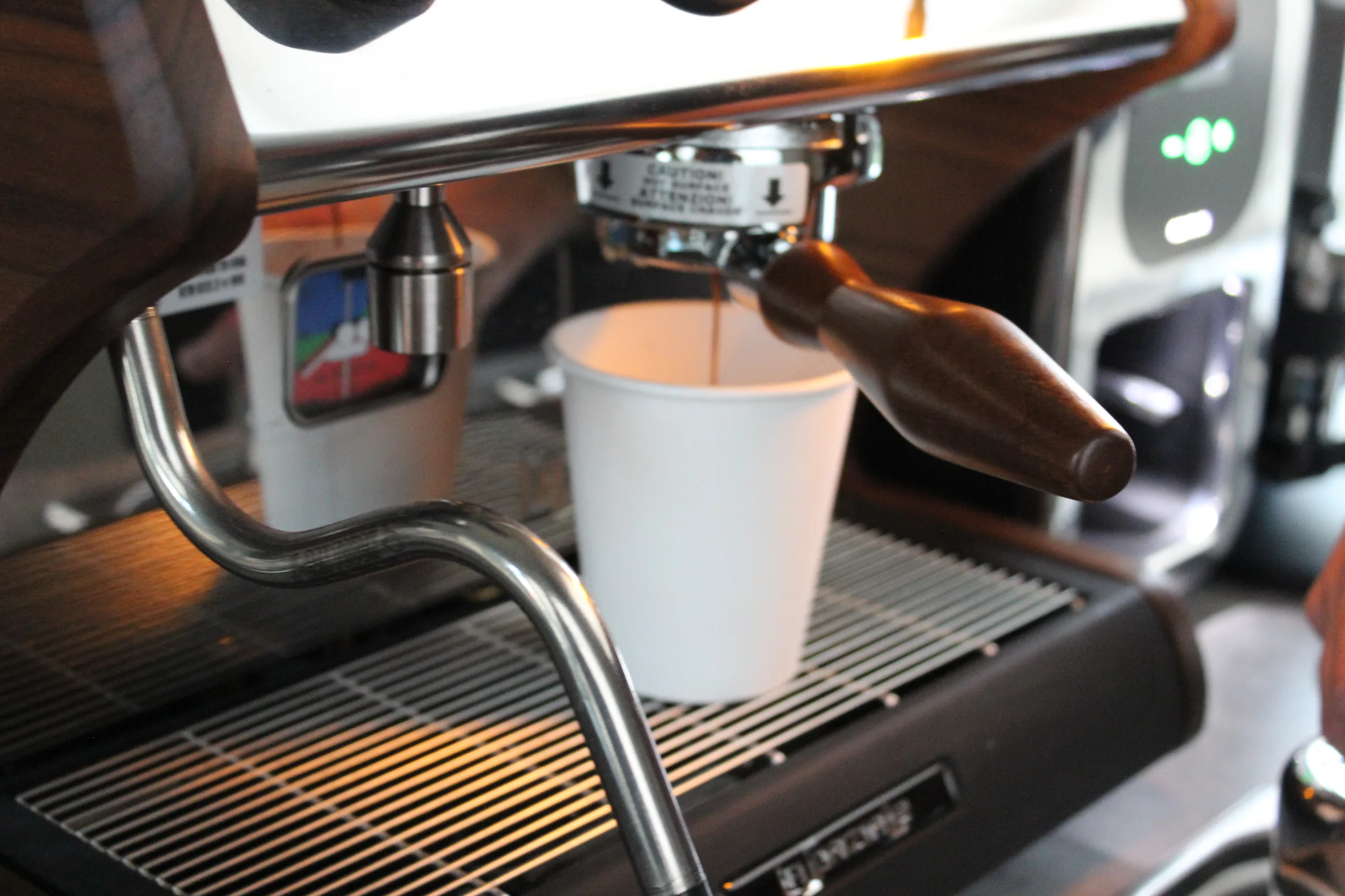 Espresso pouring from the machine into a branded Wooden Cow Coffee cup, walnut and chrome in frame